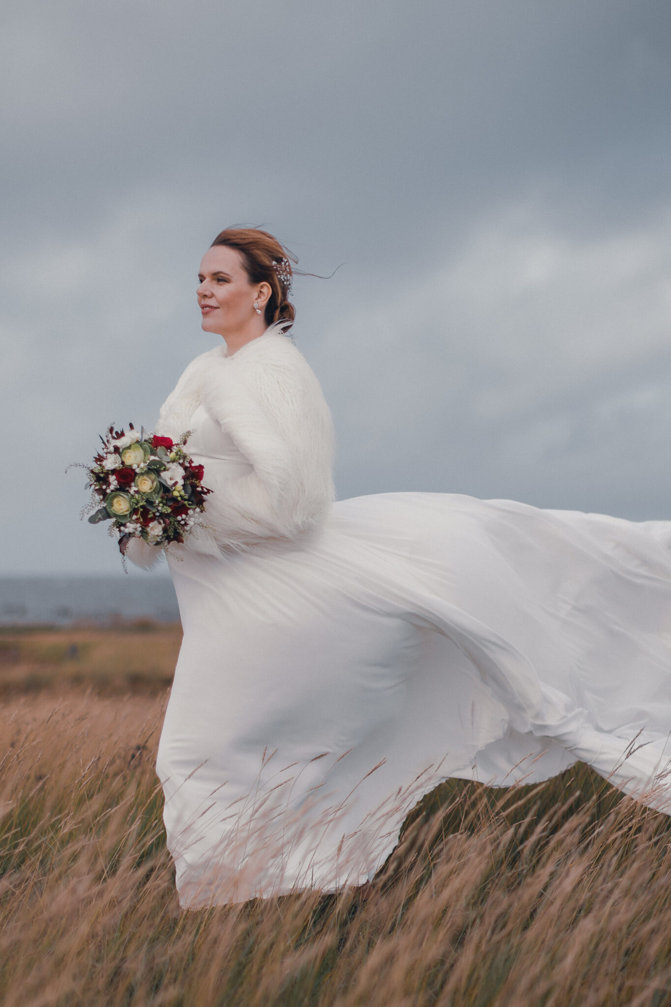 A beautiful bride in a white gown happily running through a field of tall grass.