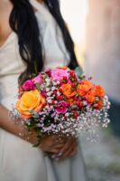 Close-up of a colorful bridal bouquet featuring orange and pink roses, red berries, and delicate baby's breath